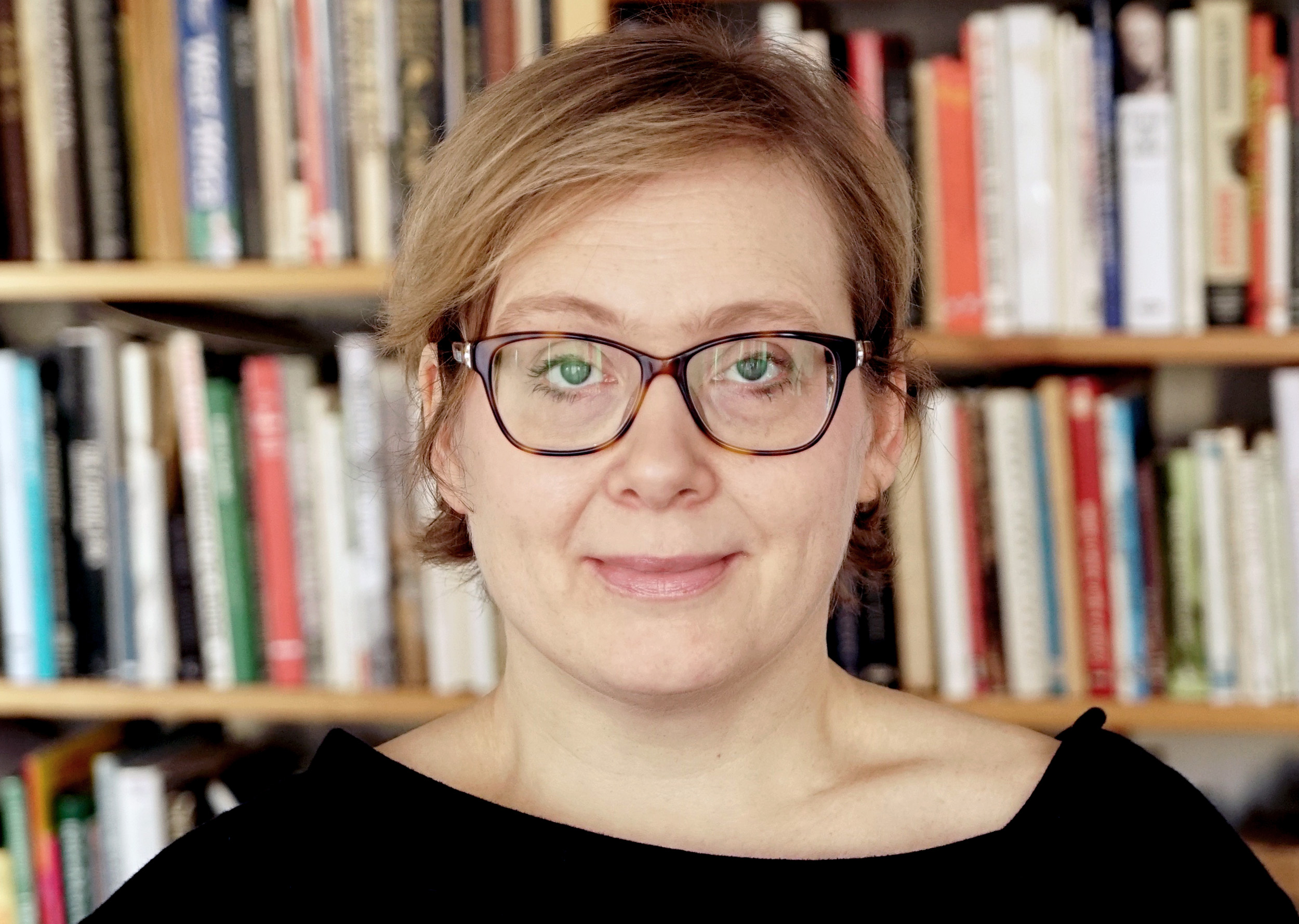 Taiteilija Maija Blåfieldin lähikuva, jossa hänen taustallaan näkyy kirjahylly.
