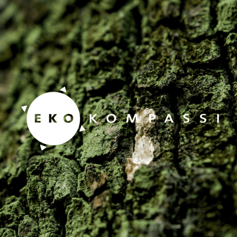 Valokuvassa sammaloitunutta puun kaarnaa ja sen päällä Ekokompassin logo.